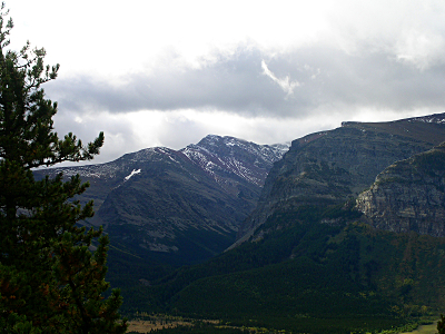 [There are two wedges of mountain which stick out side-by-side. They are huge. The far mountain has dustings of snow across the top sections.]